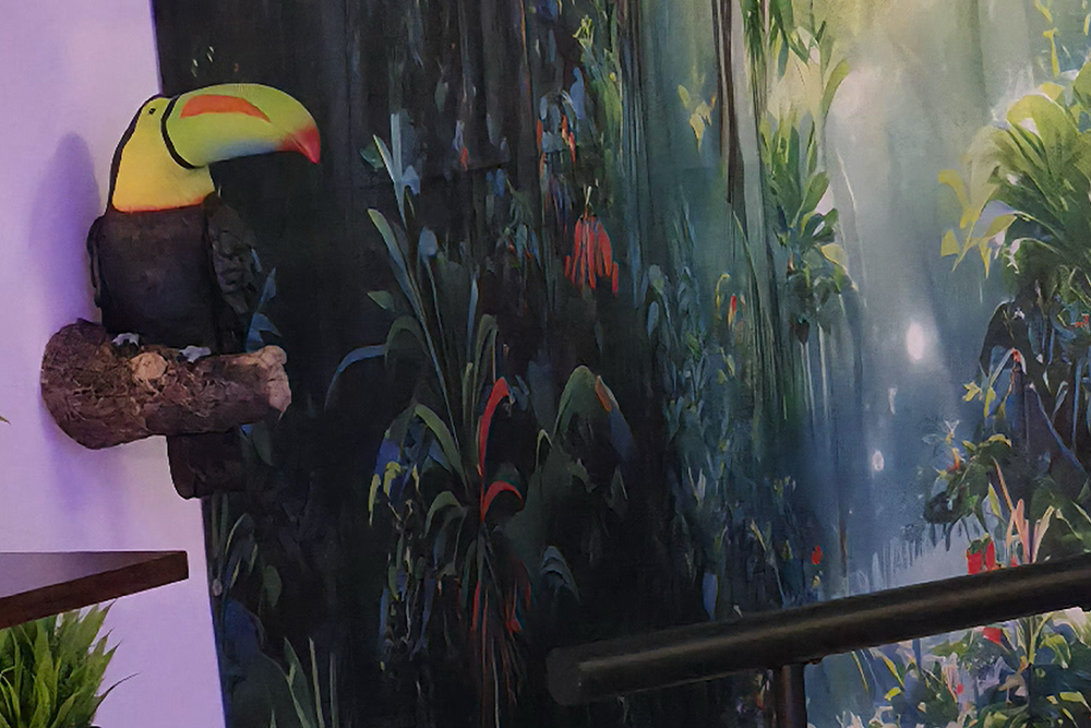 Colorful toucan plush perched on a wooden branch against a purple wall with a jungle mural.