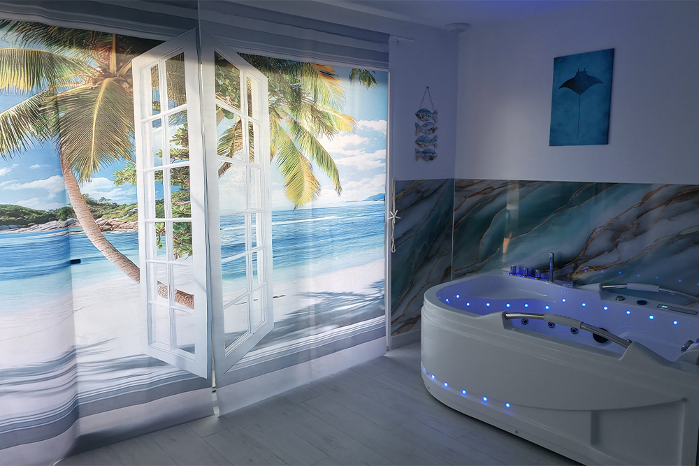 White jacuzzi tub with blue LED lights in a seaside-themed spa room featuring a large tropical beach mural and open-window wall art.