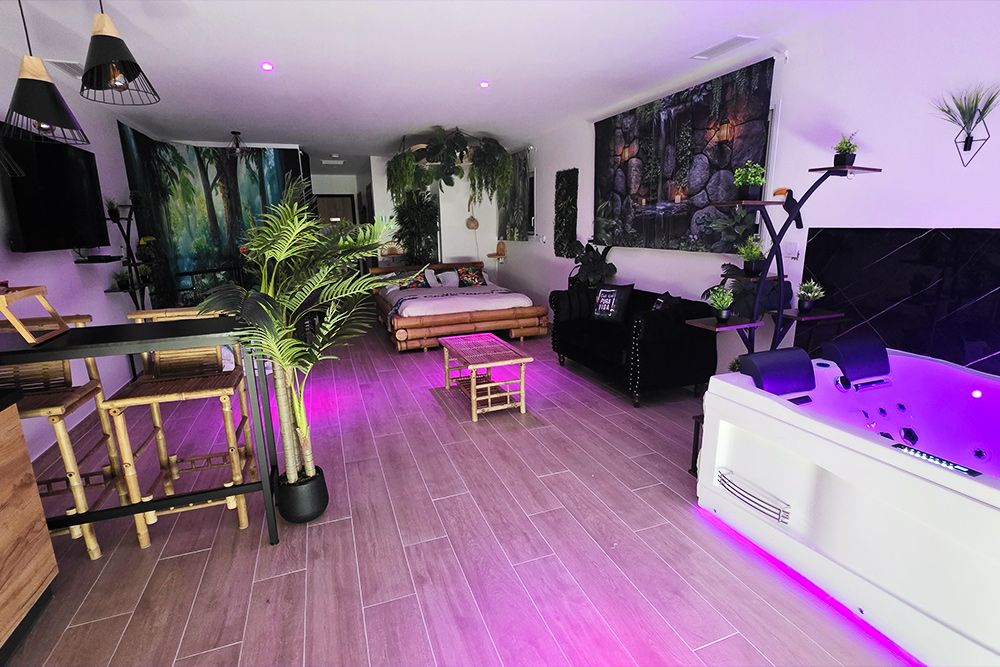 Luxurious open-plan living area with a white jetted tub, purple LED lighting, and tropical plants in a modern home.